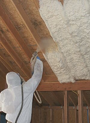 A worker spraying foam between ceiling joists.